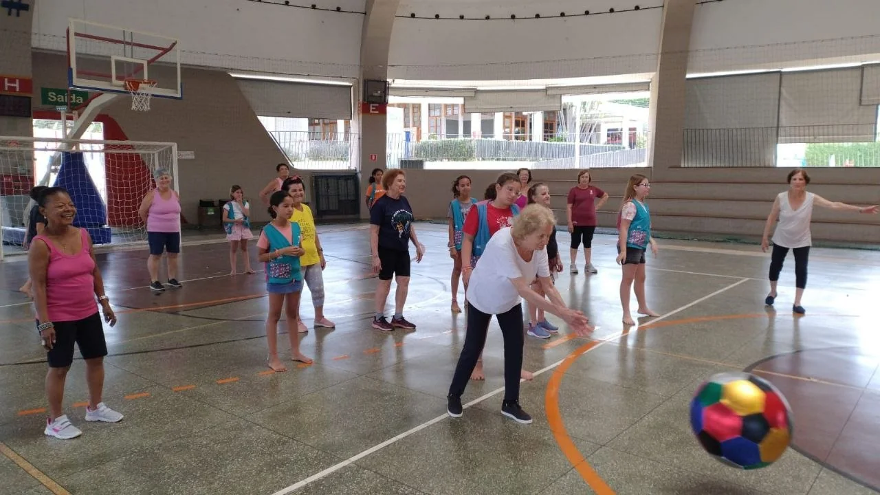 Participantes em prática corporal com bola colorida em espaço coberto